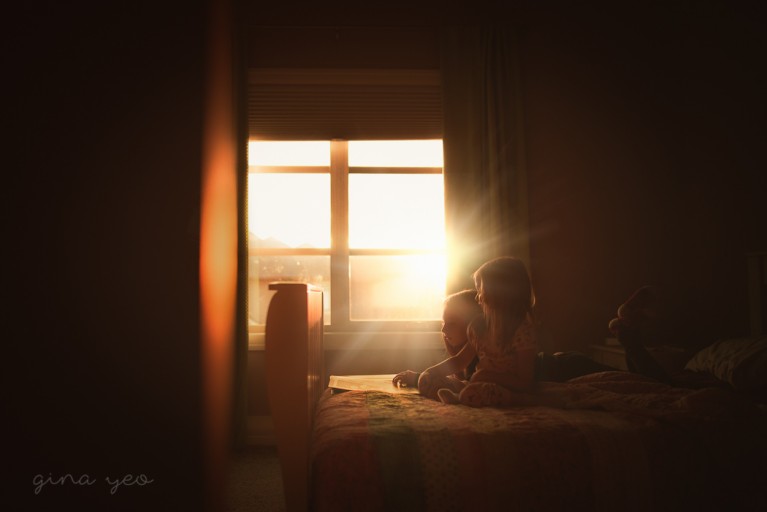 backlight photo of two girls reading on a bed by Gina Yeo