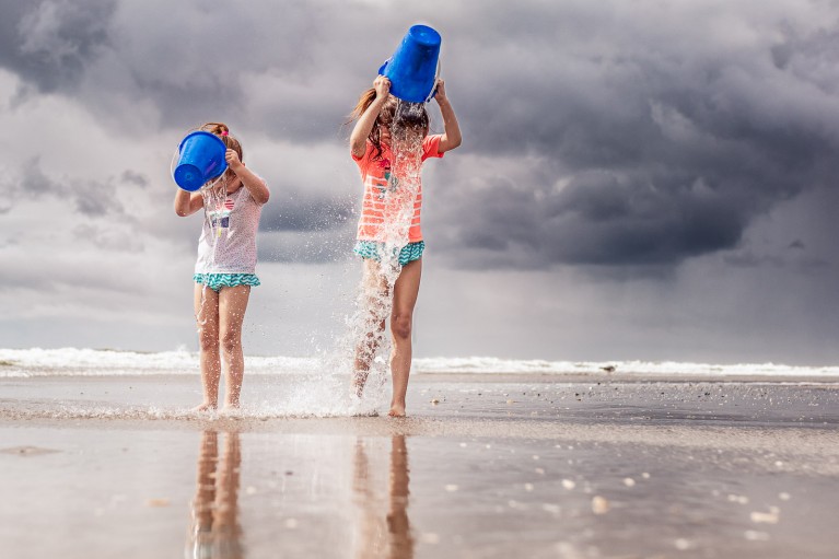 Two little girls dump buckets of water on their heads.