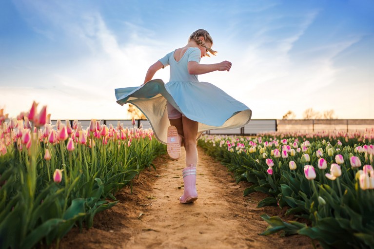 Girl running through tulip field with dramatic blue sky background