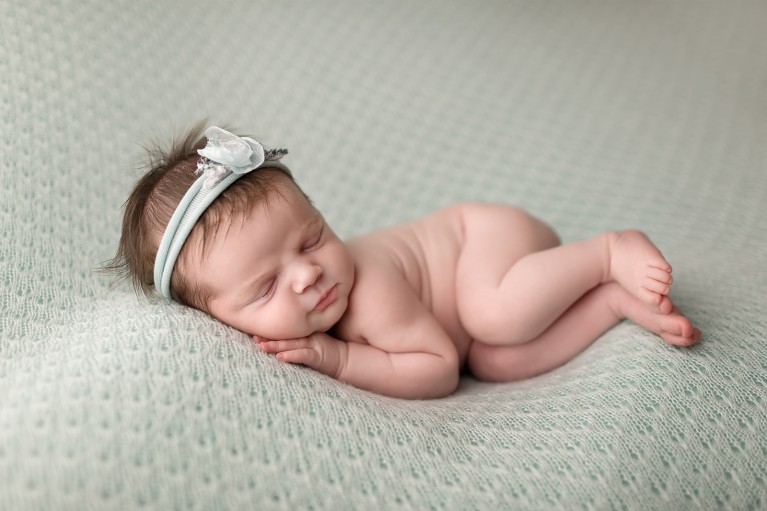 A newborn with perfectly edited skin lays on a green blanket