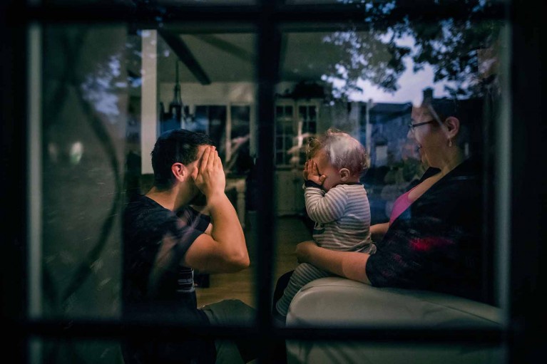 Family plays peek-a-boo, shot with creative composition through a window looking in