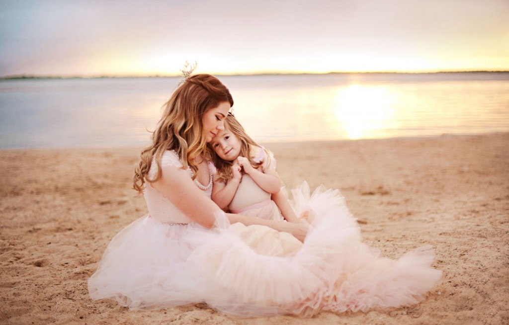 girl sitting on moms lap on the beach by Woodsy Wonders Photography