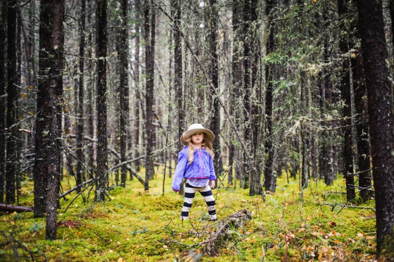 girl standing in the middle of a forrest with a hat on by Charlaine Williams