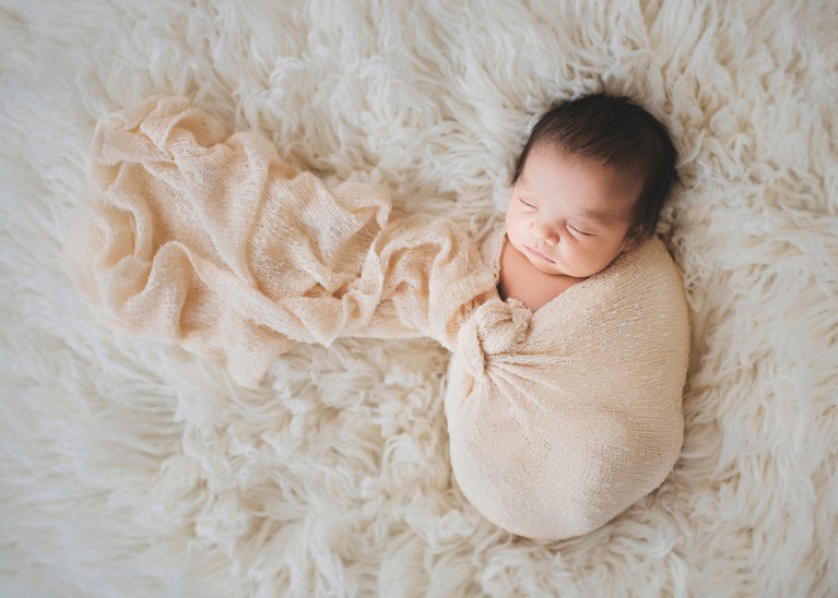 A newborn baby in a wrap posed on her back.