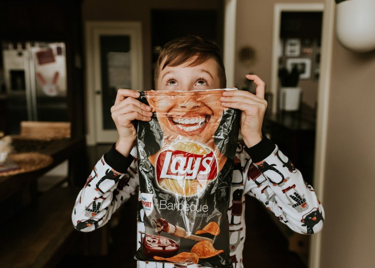 A boy holds up a bag of potato chips with a smile for a hilarious image
