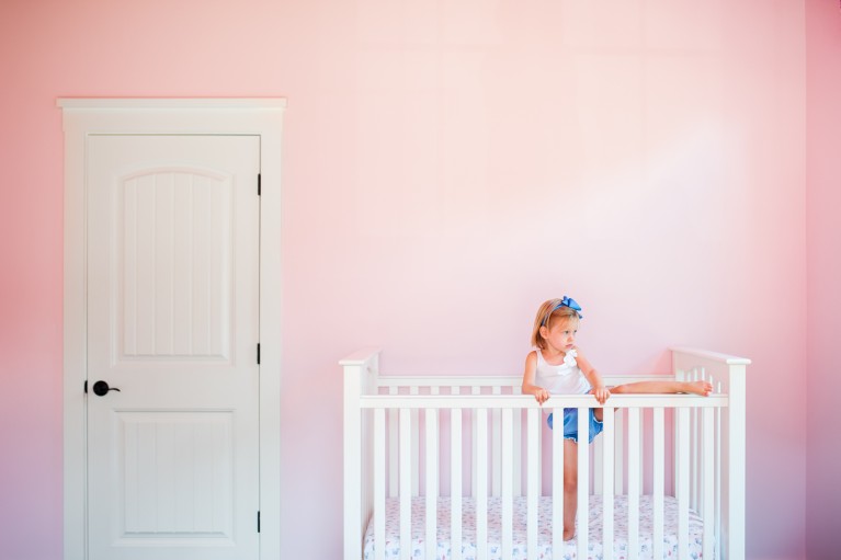 photo of girl climbing out of a crib in a pink room by Erin Konrath