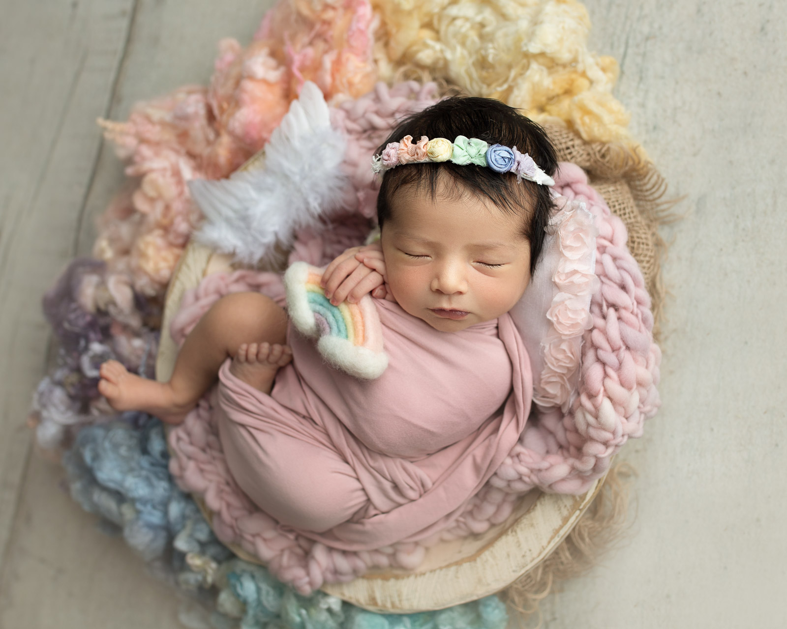 Newborn baby posed in a basket with rainbow