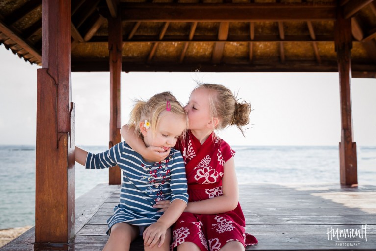 sisters sitting on a dock in Bali hugging by Rebecca Hunnicutt Farren