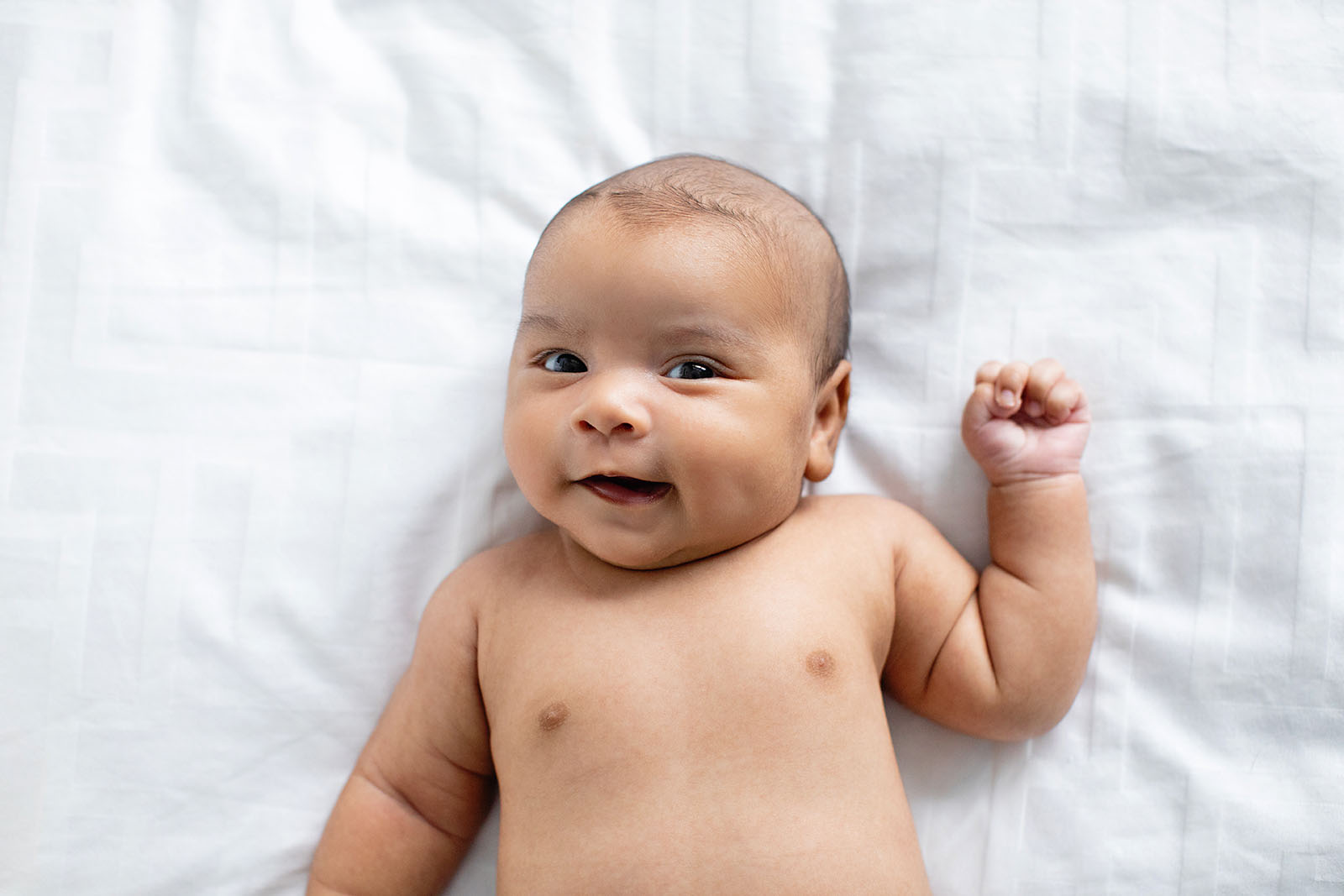 smiling-newborn-with-dimple-on-bed-in-diaper-Miami-Covid-safe-photo-session-Audrey-Blake-Photography 28 Smiling newborn baby on white sheet